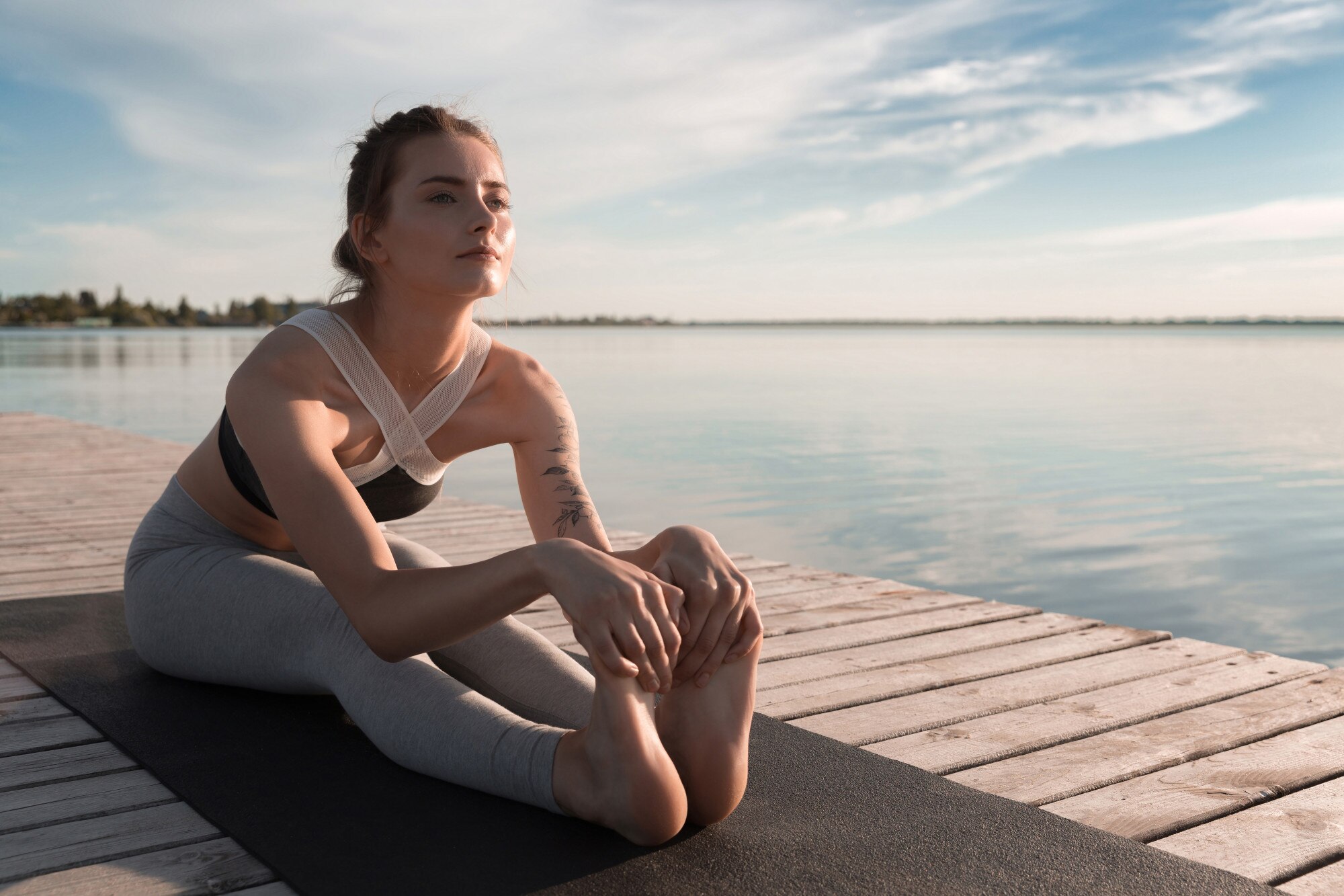 योग की मुद्रा में बैठी एक महिला, पृष्ठभूमि में प्राकृतिक परिवेश